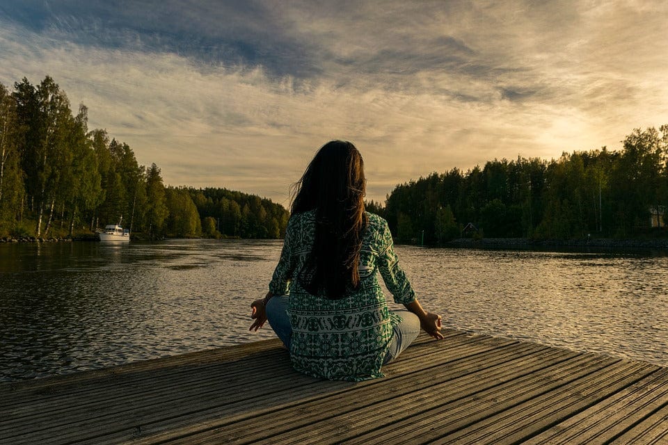 woman meditating in front of the lake
