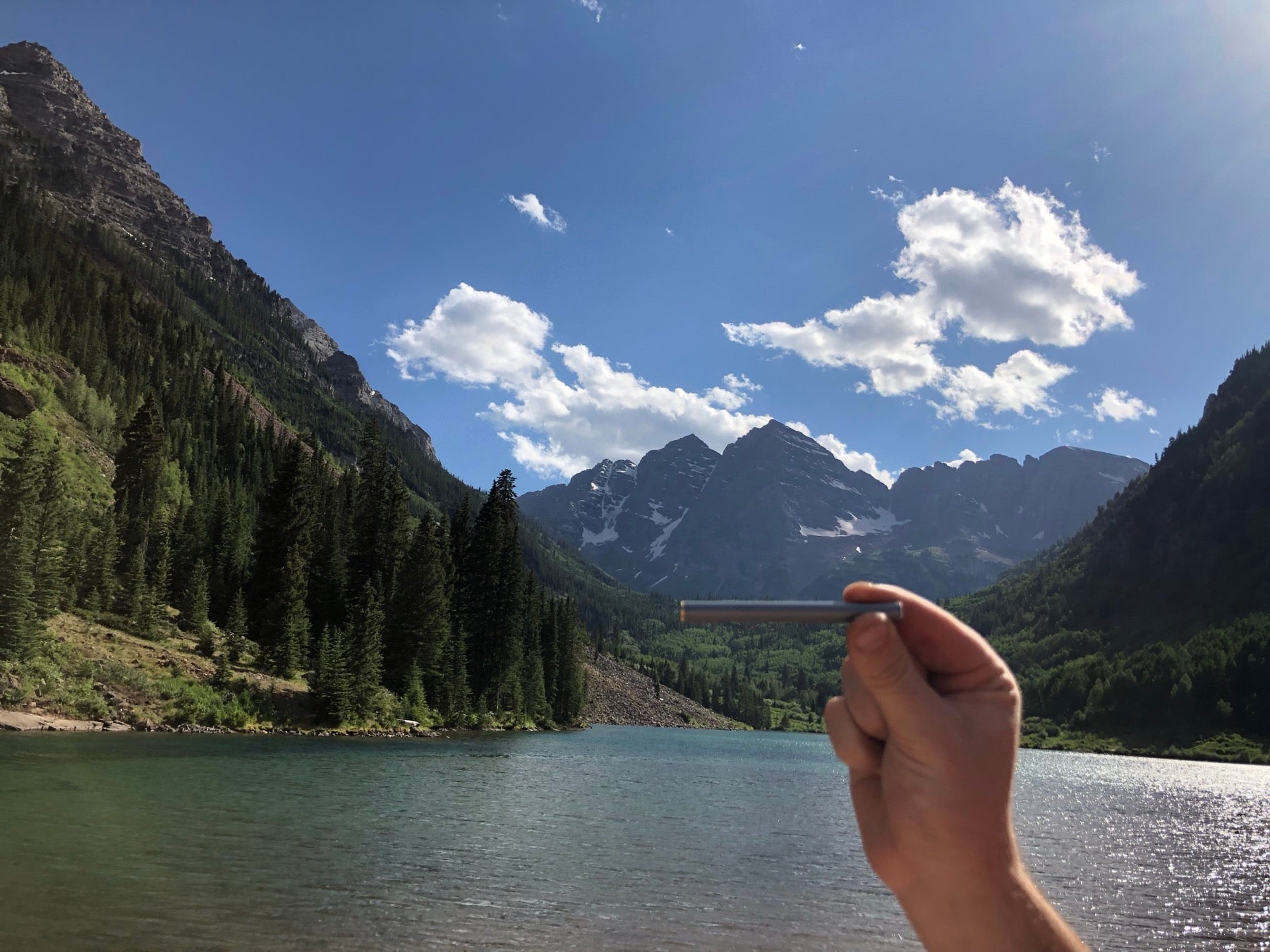 Hand holding MONQ diffuser over a mountain lake at golden hour — the portable botanical aromatherapy that brings Paleo Air to modern life
